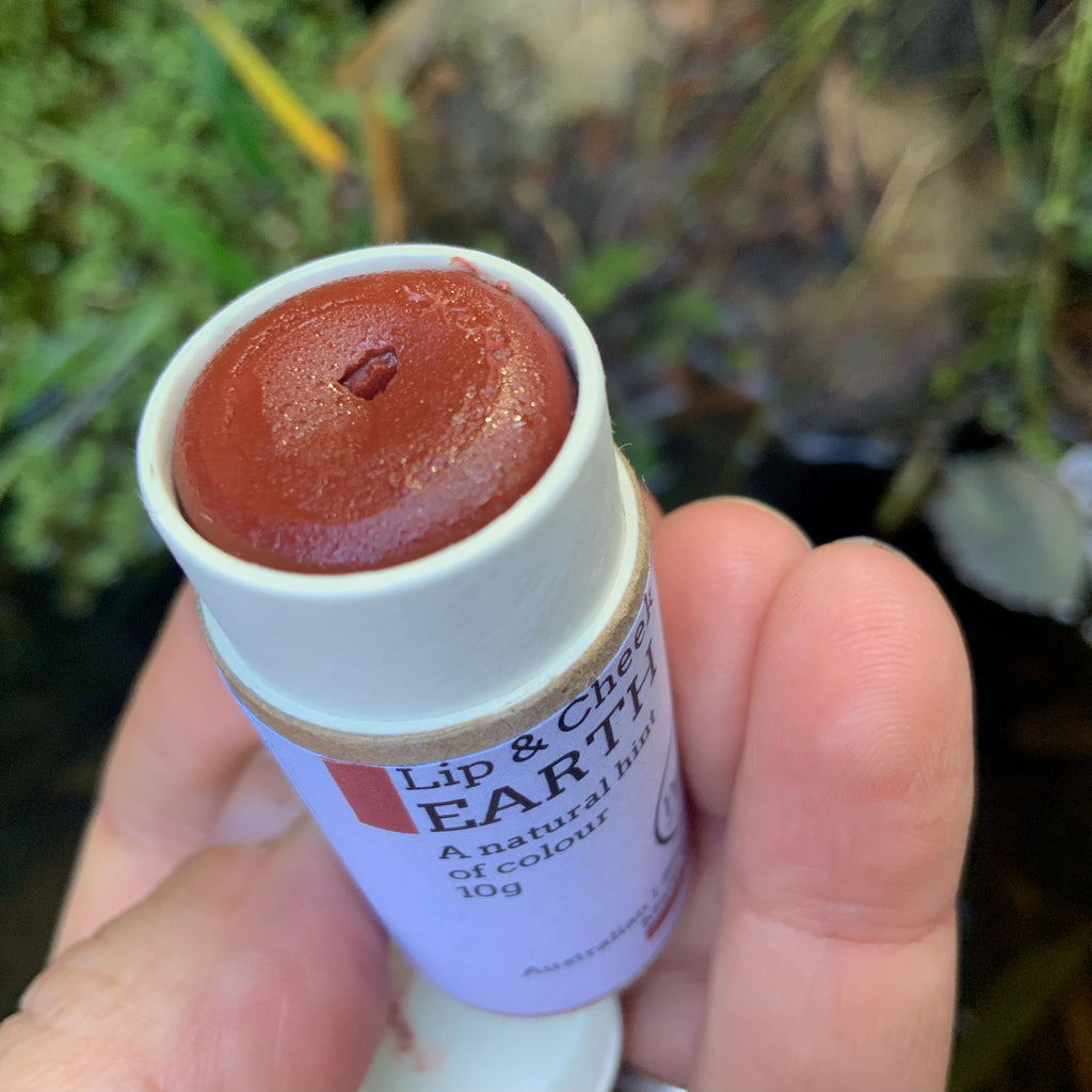 A photo of a hand holding a little cardboard tube of Earth Lip & Cheek tinted balm by Kirsty Mootz of Parva Little Things organic skincare. Available at Asiki.