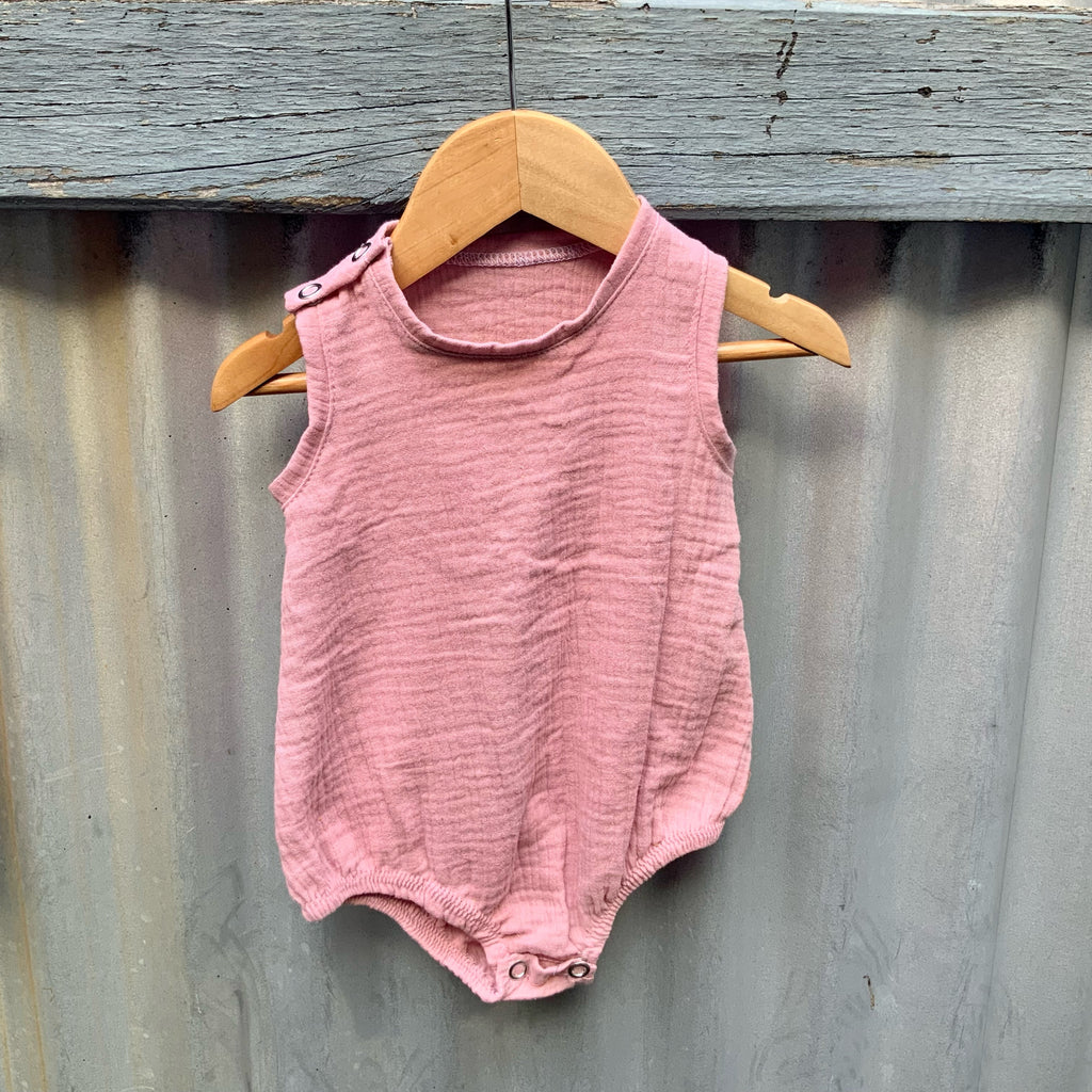 Dusty pink cotton Baby Onesie hanging on a fence. Made in Australia by Asiki.