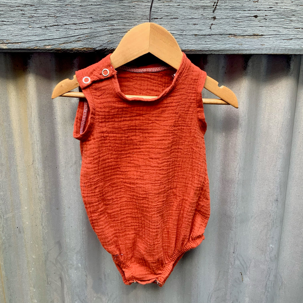 Terracotta Red cotton Baby Onesie hanging on a fence. Made in Australia by Asiki.