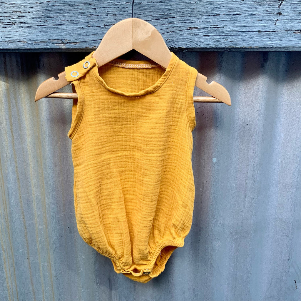 Little yellow cotton Baby Onesie hanging on a fence. Made in Australia by Asiki.