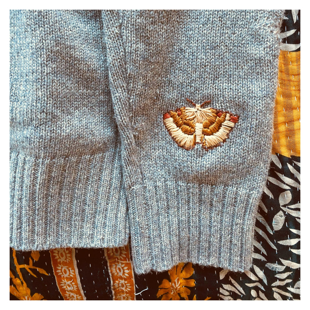 Photo of a grey jumper with a brown moth embroidered on the sleeve. The Visible Mending Embroidery Kits are available from Asiki, Australia. 